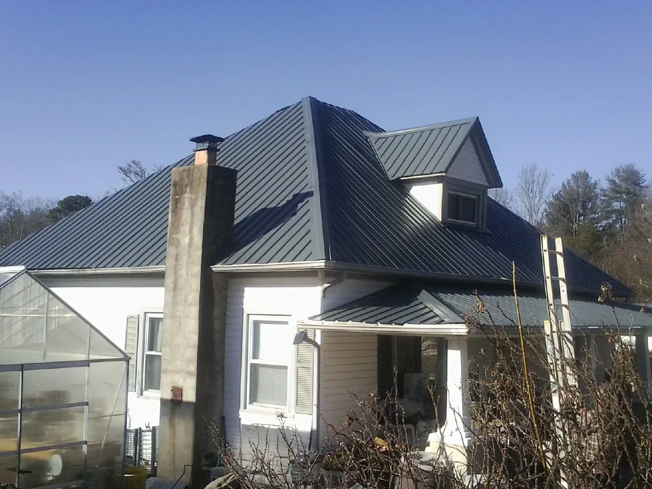 Dark blue standing seam metal roof on a white farmhouse with dormer — Slate & Tile Roof Repair by Roofing Brothers in Wimberley