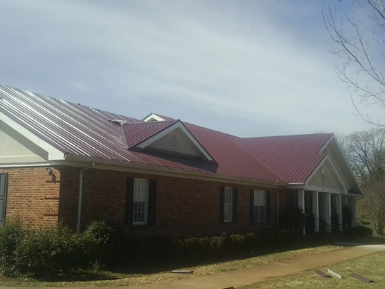 Red metal roof with gabled entries on a long brick building, from a Hail Damage Roof Repair job in Wimberley
