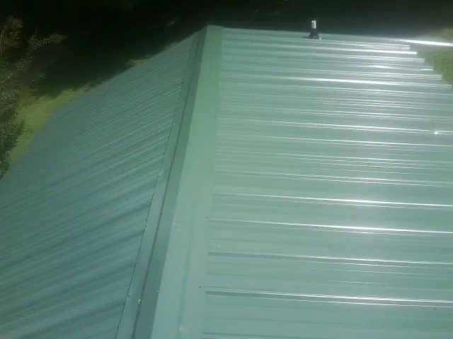 New green metal panels meeting at the ridge of a roof — Flat Roof Repair work by our crew in Wimberley