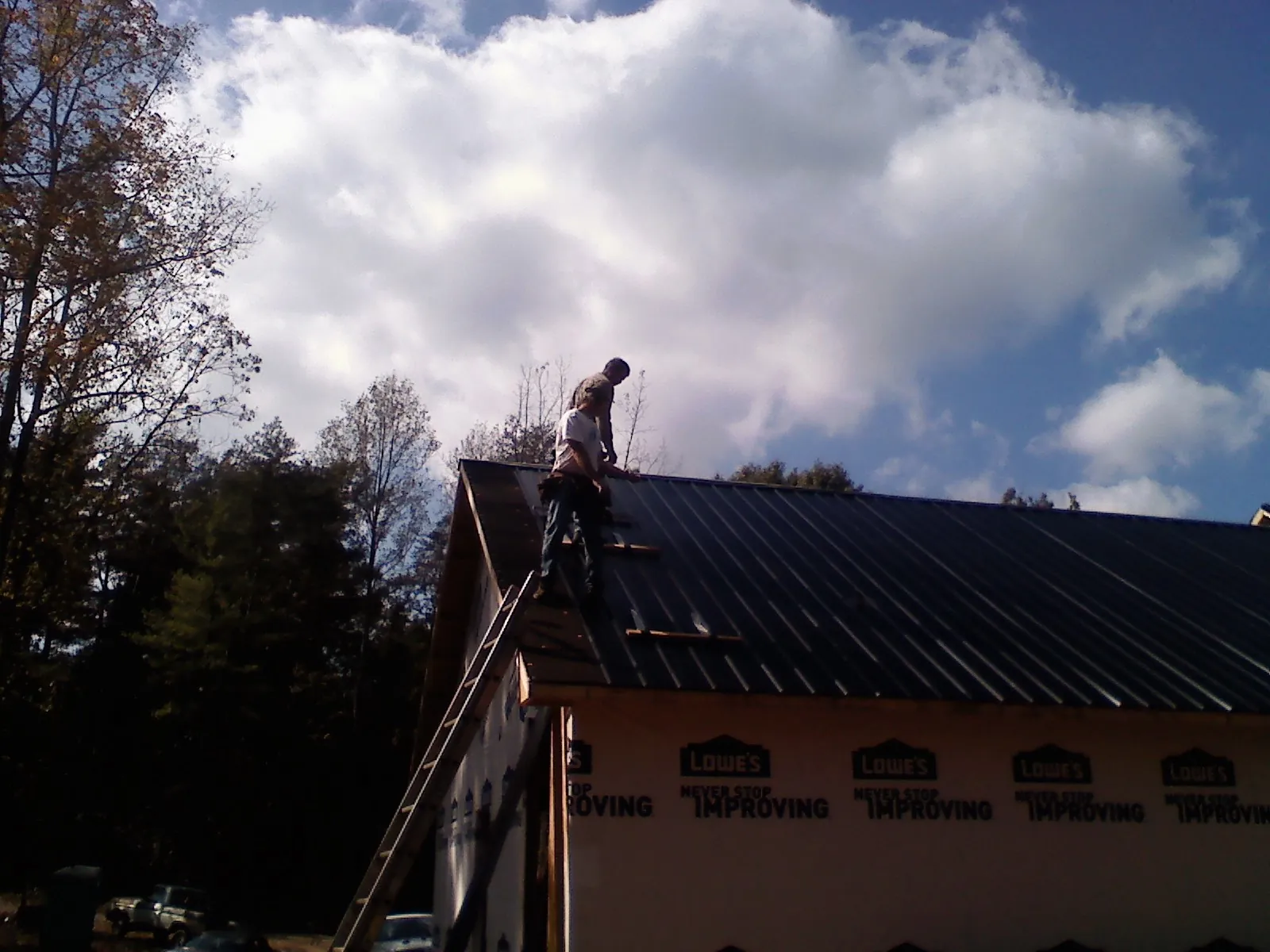 Roofer fastening dark metal panels high against a cloudy sky, from a Roof Inspection job in Wimberley