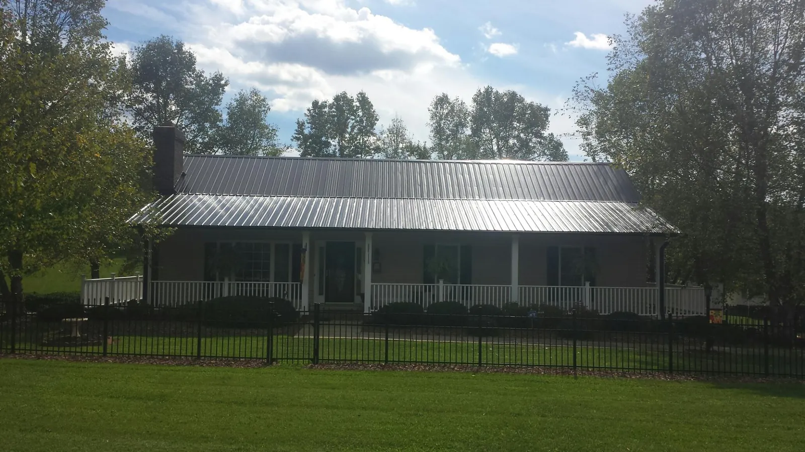 Gray metal roof on a brick ranch with a full width front porch — Gutter Guard Installation work by our crew in Wimberley