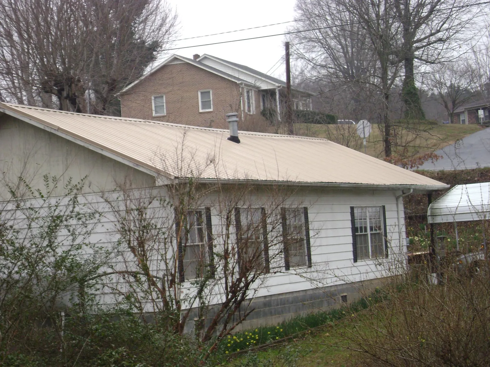 Tan metal roof on a white sided house set into a hillside — Commercial Roofing by Roofing Brothers in Wimberley